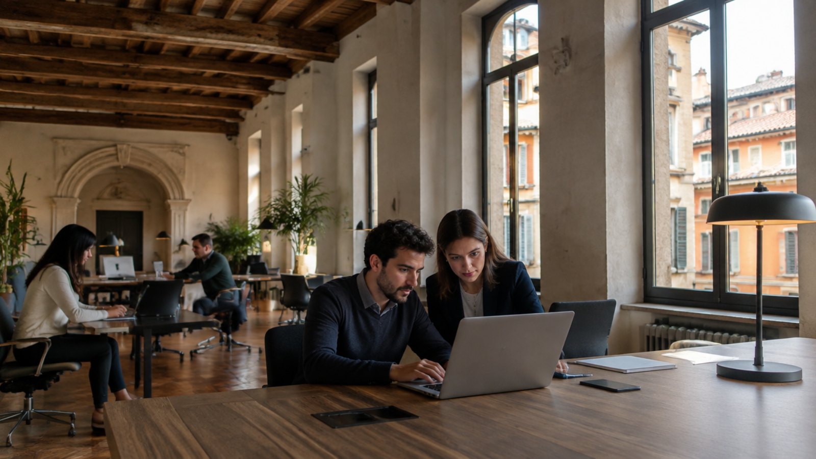 Colleagues reviewing a document on a laptop in a historic office building in Milan